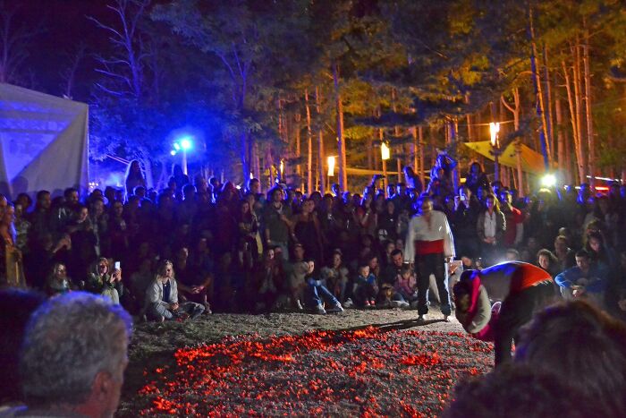 Crowd watching a dangerous historical sport involving walking on hot embers at night in an outdoor forest setting.