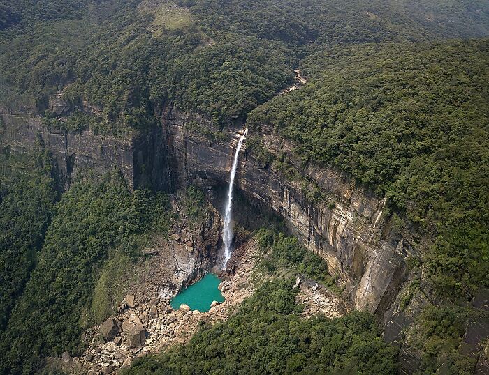 Tall waterfall cascading over rocky cliff surrounded by dense forest, showcasing incredible weather records of powerful nature.