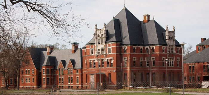 Abandoned brick building with gothic architecture surrounded by bare trees, a spooky destination for Halloween visits.