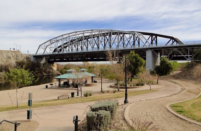 Steel bridge over a calm river with a park below, showing nature’s power and weather records on the planet.