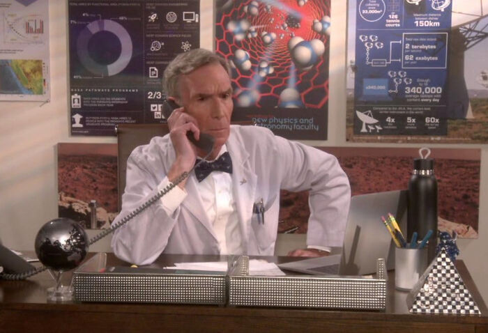 Man in white lab coat on phone in office filled with science posters, illustrating unknown things about celebrities.