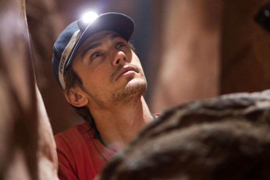 Man wearing a cap with a headlamp exploring a narrow cave, a scene from movies based on true stories.