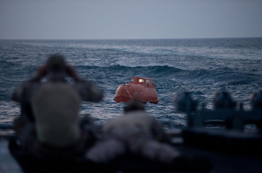 Rescue team watching an orange lifeboat in rough ocean waves in a scene from movies based on true stories.