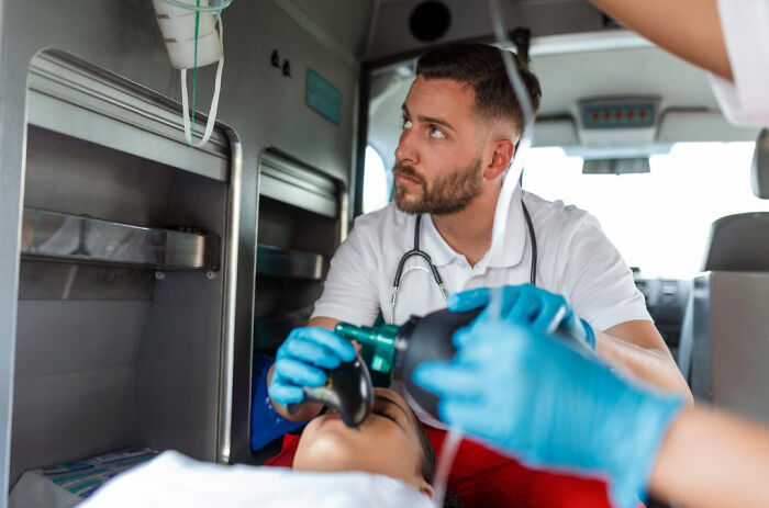 Paramedic wearing gloves assists patient with oxygen mask inside an ambulance highlighting cancer survivors symptoms.