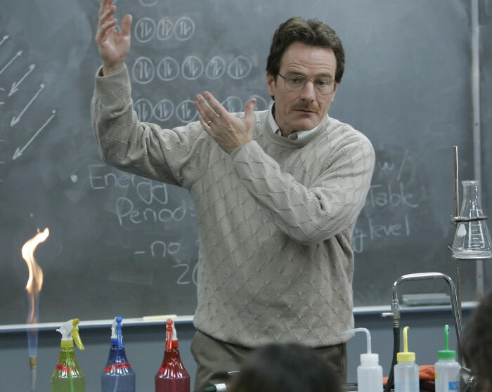 Man in glasses and sweater demonstrating chemistry experiment in classroom, related to unknown things about celebrities.