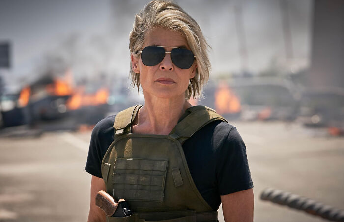 Actress in tactical gear and sunglasses on a fiery set, illustrating unknown things about celebrities from firsthand encounters.