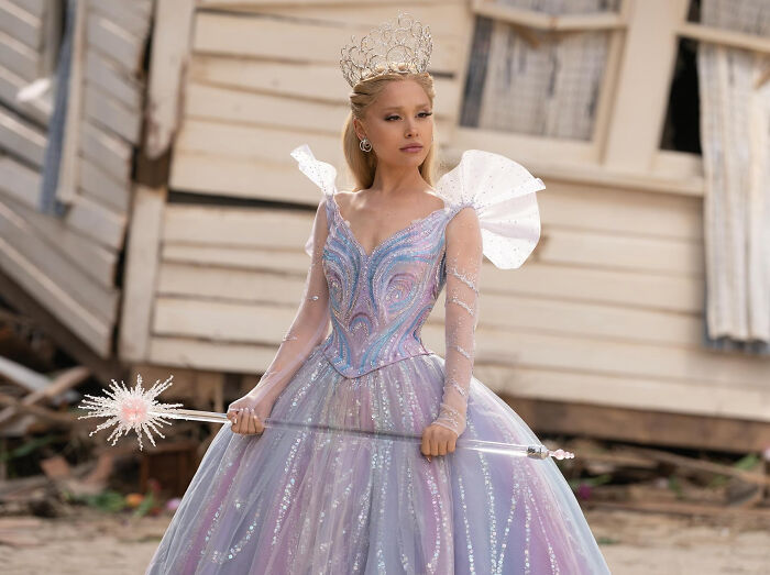 Young woman in an elaborate sparkling dress and crown holding a wand, representing unknown things about celebrities.