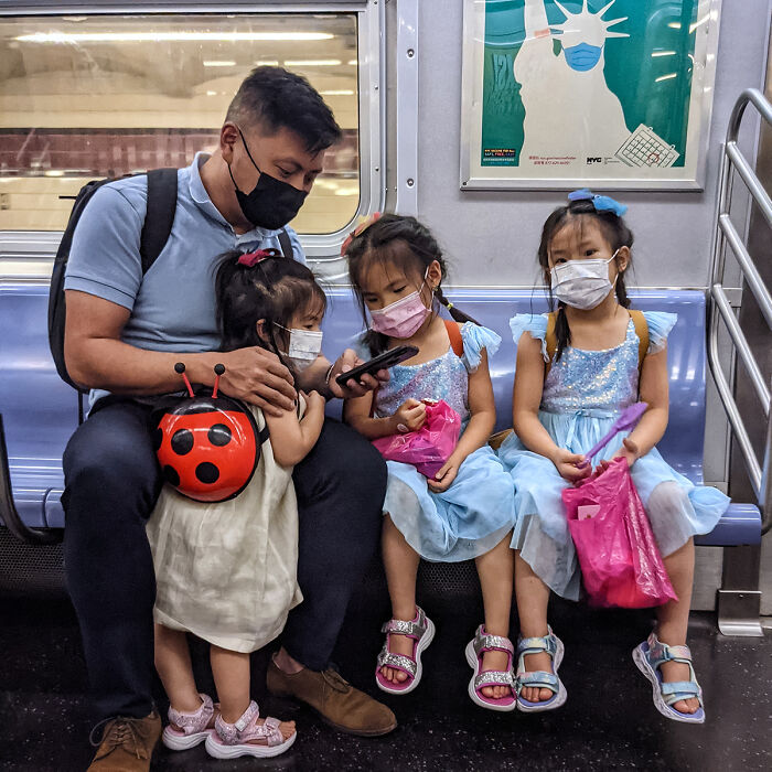 Father and three young girls wearing masks and colorful dresses captured in a street portrait on NYC subway.