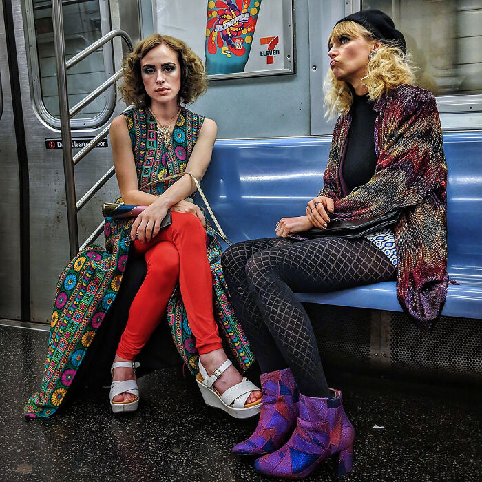 Two stylish women wearing colorful outfits and seated inside a NYC subway, capturing street portraits underground.