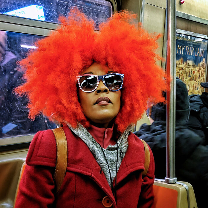 Woman with bright red hair and star-spangled sunglasses wearing a red coat in a captivating NYC subway street portrait.