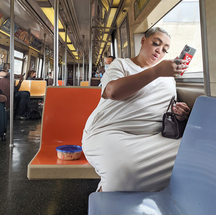 Woman wearing white dress using phone inside NYC subway, captured in street portrait showing life underground.