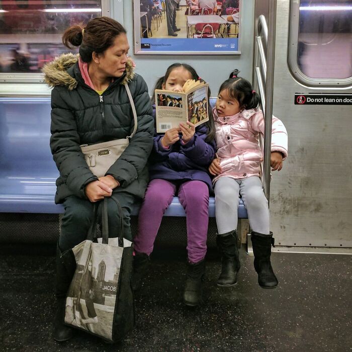 Woman and two children sitting in NYC subway, one child reading a book, captured in street portraits underground.