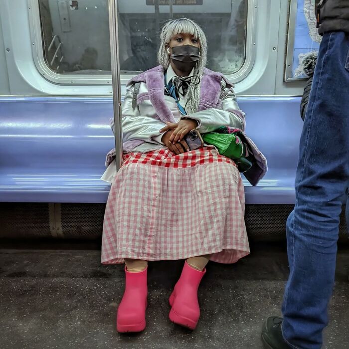 Young woman in bright pink boots and patterned skirt sitting in NYC subway, a striking street portrait capturing life underground.