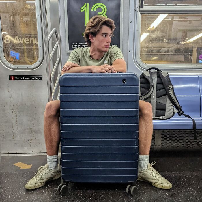 Young man sitting in NYC subway with large suitcase and backpack, a candid street portrait capturing life underground.