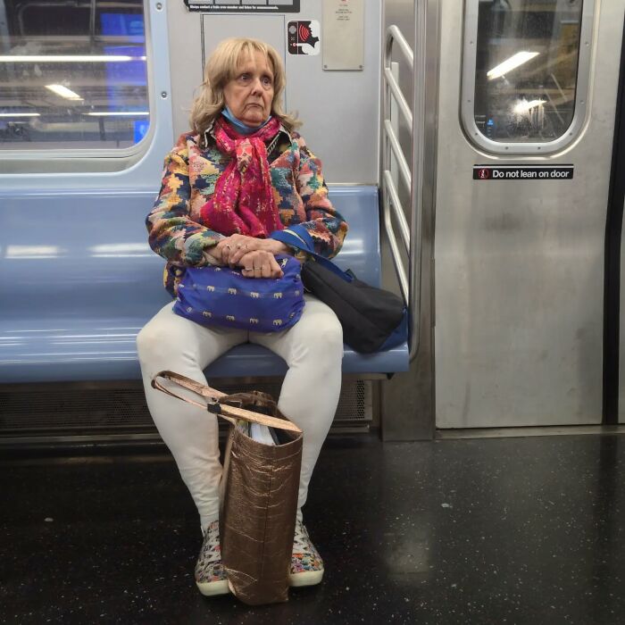 Elderly woman wearing colorful jacket and scarf, sitting on NYC subway bench in a candid street portrait.