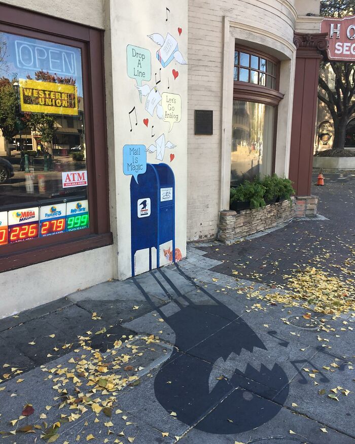 Shadow art installation of a mailbox casting a monster shadow on the sidewalk, blending ordinary objects with clever art.