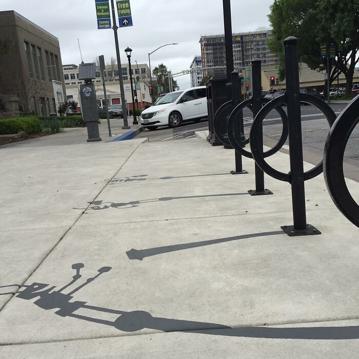 Shadow art installation on a city sidewalk creatively transforming bike racks into vintage telephones with painted shadows.