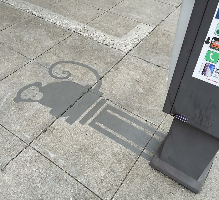 Shadow art installation on sidewalk using a utility box, creating the clever silhouette of a monkey with a curled tail.