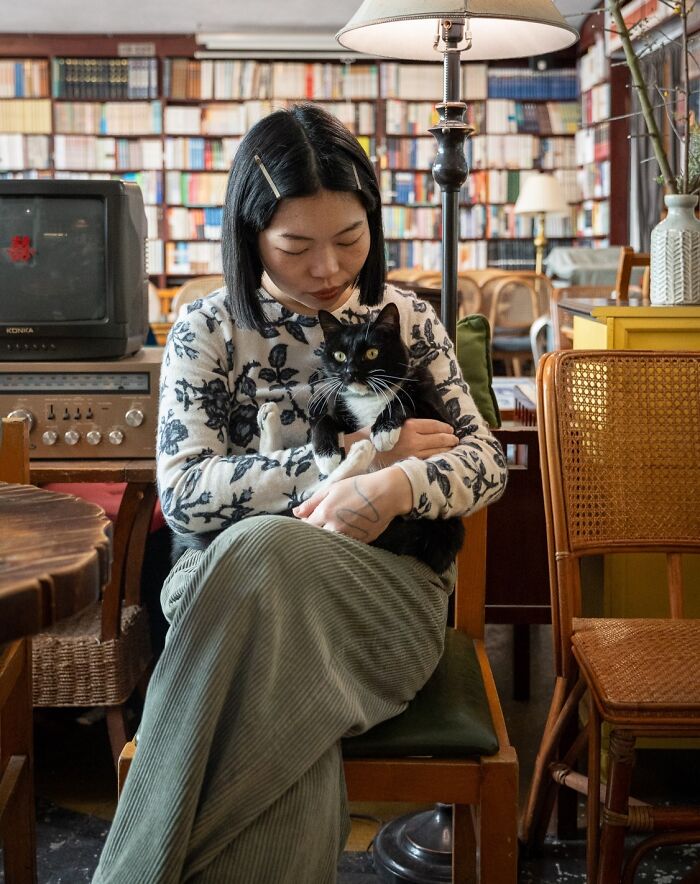 Woman holding a black and white cat in a cozy urban setting, showcasing cats adapted to city life by a photographer.
