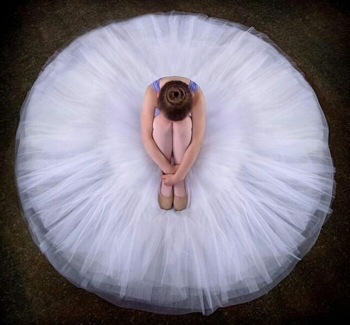 Young ballet dancer in a white tutu sitting curled up, showcasing beautiful childhood moments shared worldwide.