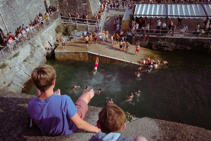 Children swimming and diving in a natural pool with a crowd watching, capturing beautiful childhood moments worldwide.
