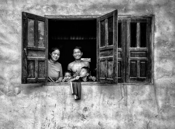 Family with children smiling together at rustic window, capturing beautiful childhood moments around the world in black and white.