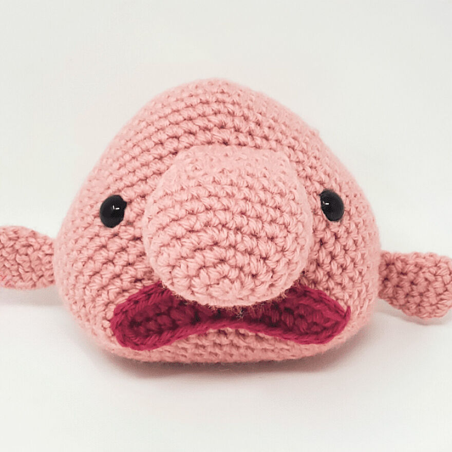 Crochet animal with large nose and expressive face, handmade with pink and red yarn, showcasing unique personality.