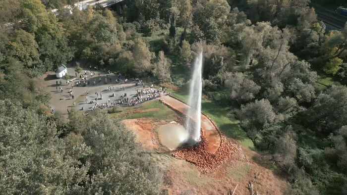 A powerful water geyser erupting amid dense trees with crowds observing, showcasing incredible weather records.