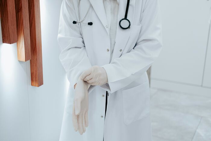 Doctor in white coat with stethoscope putting on gloves preparing for patient consultation first opinions