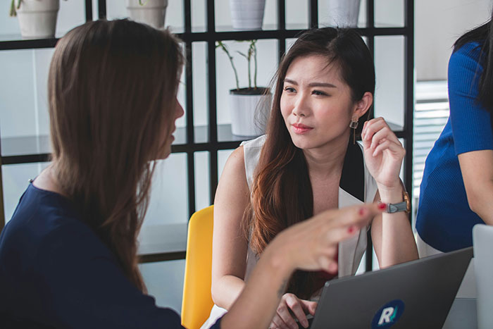 Two women discussing in an office setting with laptop, illustrating AI scored job interview in real time technology use. Two women discussing in an office setting with laptop, illustrating AI scored job interview in real time technology use.
