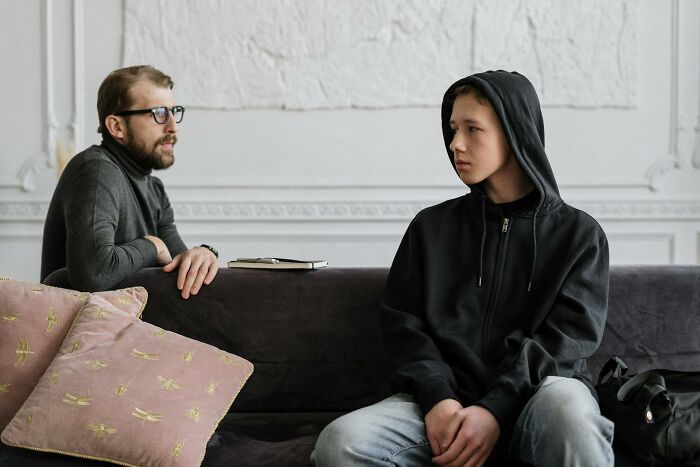 Man and teenage son sitting on a couch in a house, engaged in a serious family relationship conversation.