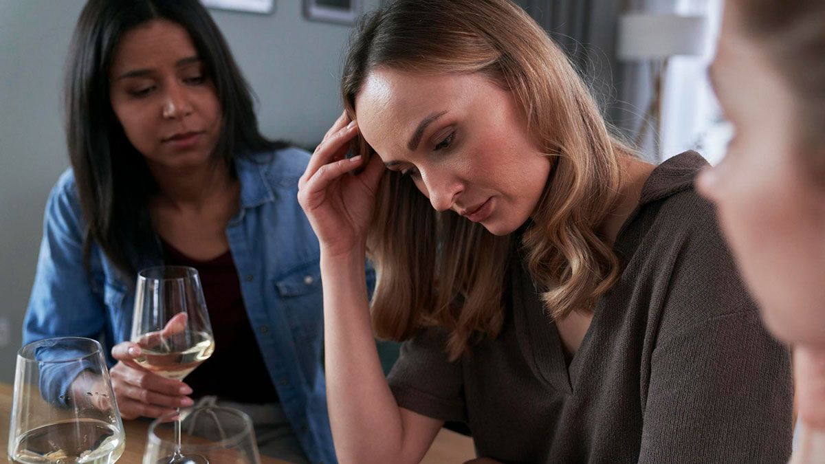 Woman upset at dinner table with two others, tense atmosphere hinting at conflict over racist slurs by BIL.