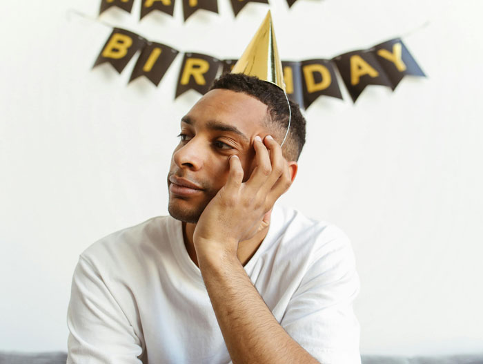 Young man wearing a party hat, looking away thoughtfully at a birthday party, representing an annoying toxic friend photographer.