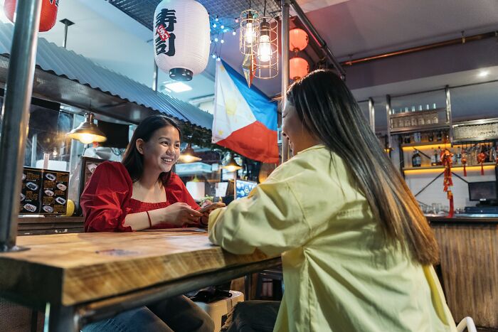 Two women enjoying a lively conversation at a restaurant decorated with cultural lanterns and a national flag, showcasing positive stereotypes.