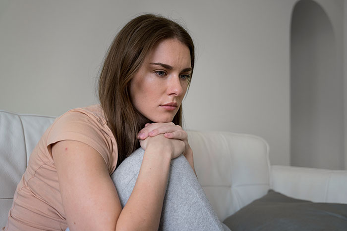 Woman sitting on couch with worried expression, reflecting concern over 11-year-old acting creepy around stepsister.