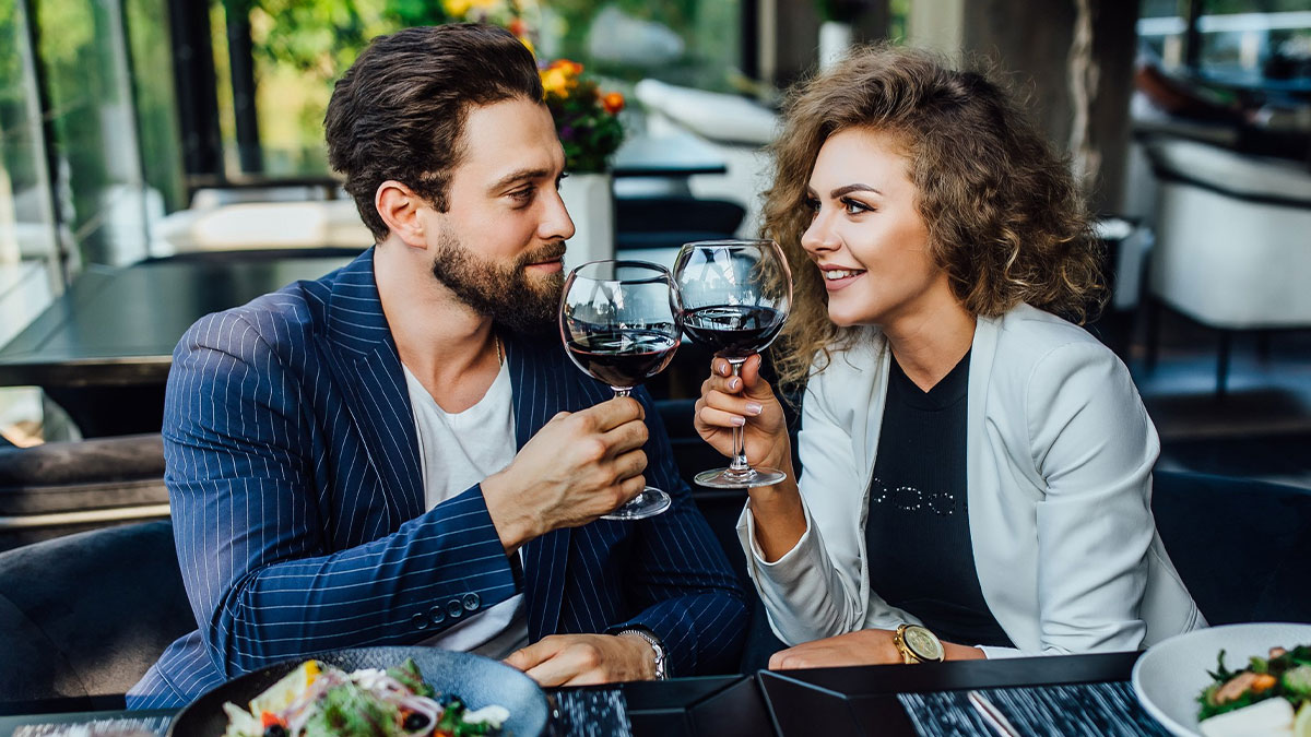 Couple enjoying a restaurant meal, toasting with red wine glasses in an elegant dining setting.