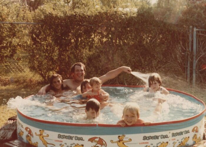 Family photo in a small Scooby-Doo pool with kids and adults splashing and playing outdoors on a sunny day.