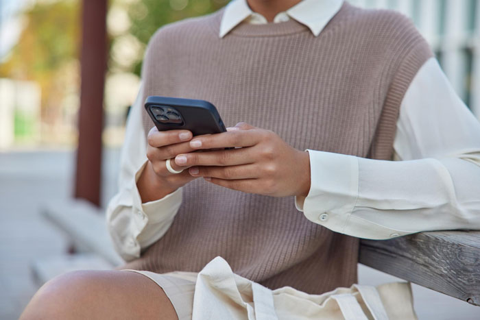 Woman wearing brown sweater vest using phone outdoors, illustrating entitled lady mad about grandkid relationship issues.