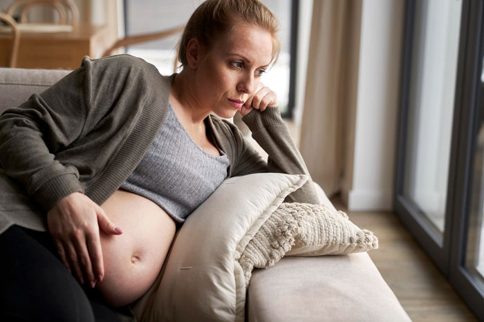 Pregnant woman lying on a couch looking thoughtful, representing an entitled lady upset about grandkid naming and relationship.