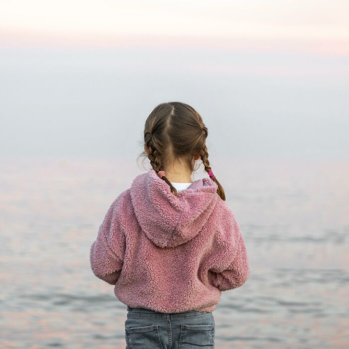 Child in a pink hoodie looking at the calm sea, symbolizing hope and cancer survivors sharing unexpected symptoms.