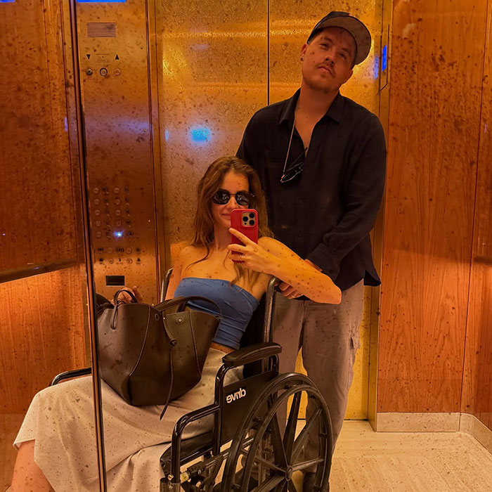 Woman in wheelchair taking selfie with man behind her in elevator, highlighting dark sides of Victoria’s Secret models. Woman in wheelchair taking selfie with man behind her in elevator, highlighting dark sides of Victoria’s Secret models.