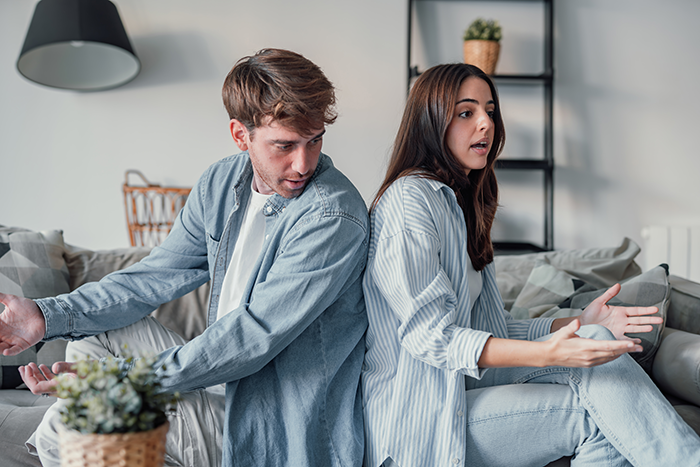 Young couple arguing on couch, tense relationship showing boyfriend lying and extorting money under false pretenses. Young couple arguing on couch, tense relationship showing boyfriend lying and extorting money under false pretenses.