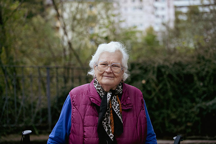 Elderly woman outdoors wearing glasses and a purple vest, representing family care and refusal to take responsibility. Elderly woman outdoors wearing glasses and a purple vest, representing family care and refusal to take responsibility.