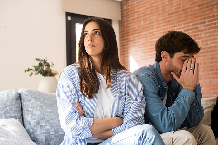 Couple sitting apart looking upset, illustrating guy fearing best man may go after his girlfriend after ex-wife's cheating. Couple sitting apart looking upset, illustrating guy fearing best man may go after his girlfriend after ex-wife's cheating.