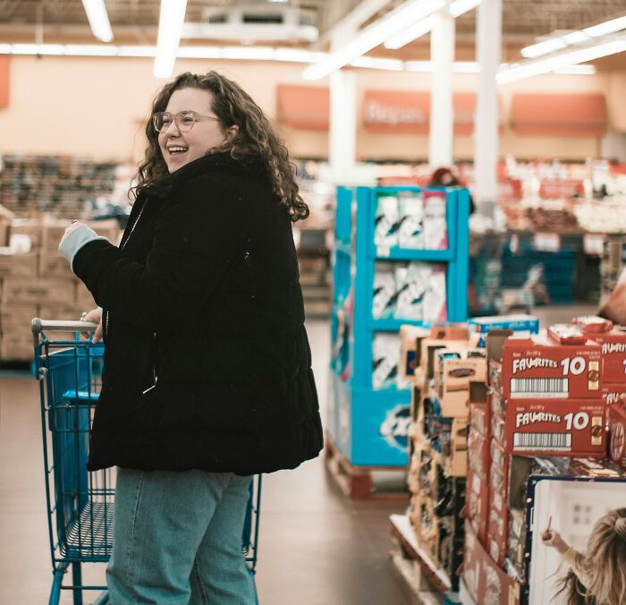 Pregnant woman smiling happily while shopping in a store aisle filled with various packaged goods on shelves. Pregnant woman smiling happily while shopping in a store aisle filled with various packaged goods on shelves.