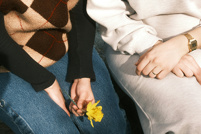 Two women sitting close, one holding a yellow flower, symbolizing the end of a friendship with 5 kids and 4 dads. Two women sitting close, one holding a yellow flower, symbolizing the end of a friendship with 5 kids and 4 dads.