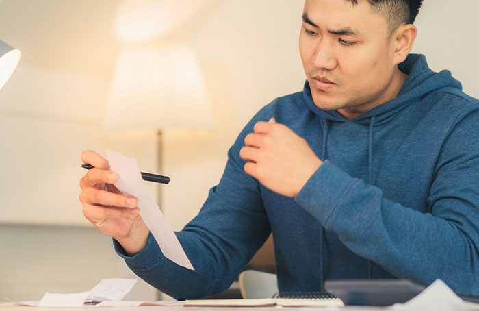 Man in blue hoodie examining papers closely, accidentally discovering loopholes and using them to his advantage.