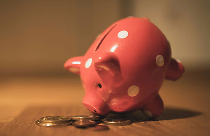 Pink piggy bank with white polka dots leaning toward a few coins on a wooden surface, illustrating loopholes concept.
