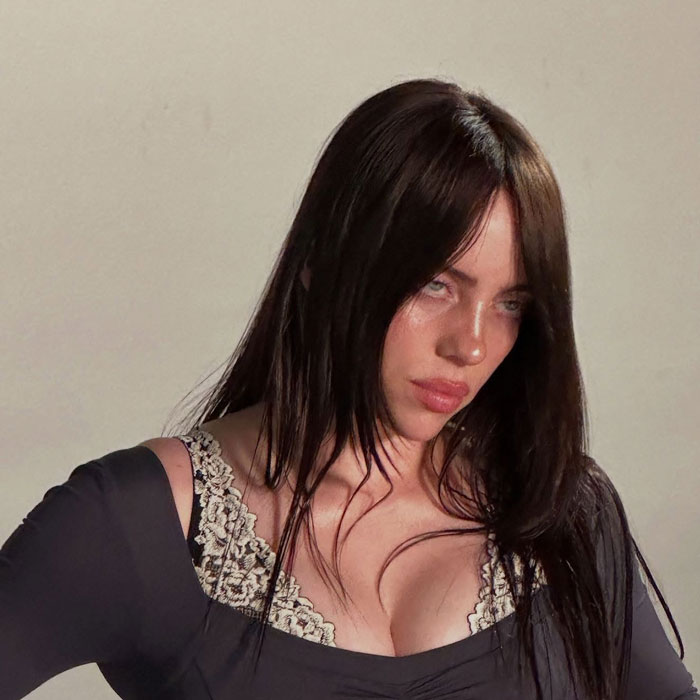 Billie Eilish with dark hair and lace top looking serious in a close-up photo related to Miami concert incident. Billie Eilish with dark hair and lace top looking serious in a close-up photo related to Miami concert incident.