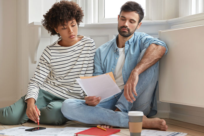 Couple sitting on floor reviewing documents, discussing wedding plans and expenses before canceling due to child-free policy. Couple sitting on floor reviewing documents, discussing wedding plans and expenses before canceling due to child-free policy.